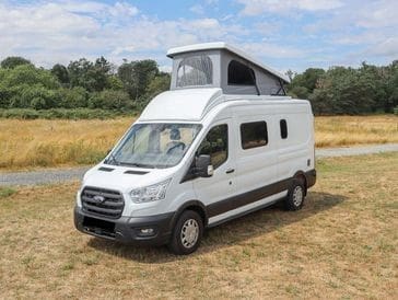 A white van parked in the grass near some trees.