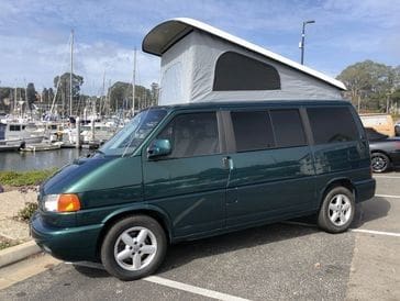 A green van parked in the parking lot with a roof up.